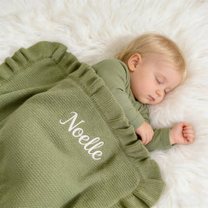 Baby asleep under a sage ruffle blanket embroidered with Noelle