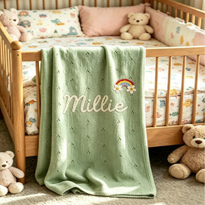 Green eyelet knit blanket embroidered with Millie and a rainbow on a crib