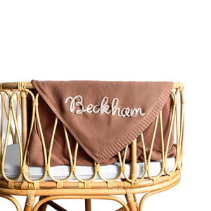 Brown knit baby blanket embroidered with Beckham on a rattan crib