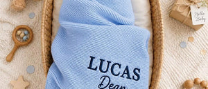 Baby wrapped in a blue knit blanket embroidered with Lucas Dean