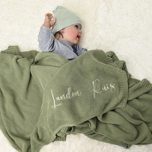 Baby under a sage knit blanket embroidered with Landon Ruis