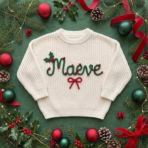 Personalized Christmas sweater with hand embroidered holly berry name & bow among Christmas decorations