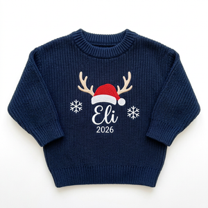 Machine embroidered reindeer antlers & Santa hat with year baby Christmas sweater on a plain background