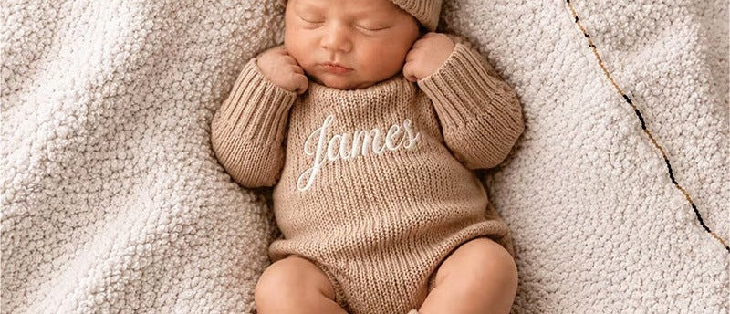 Sleeping baby in an oatmeal knit romper embroidered with James