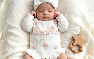 Newborn in a white ruffle knit romper embroidered with Sophia and pink flowers