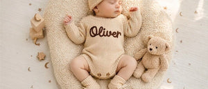 Newborn in an oatmeal knit romper embroidered with the name Oliver
