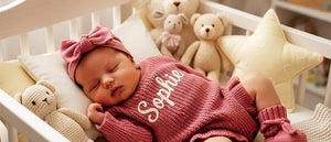 Newborn sleeping in a rose pink knit romper embroidered with the name Sophia