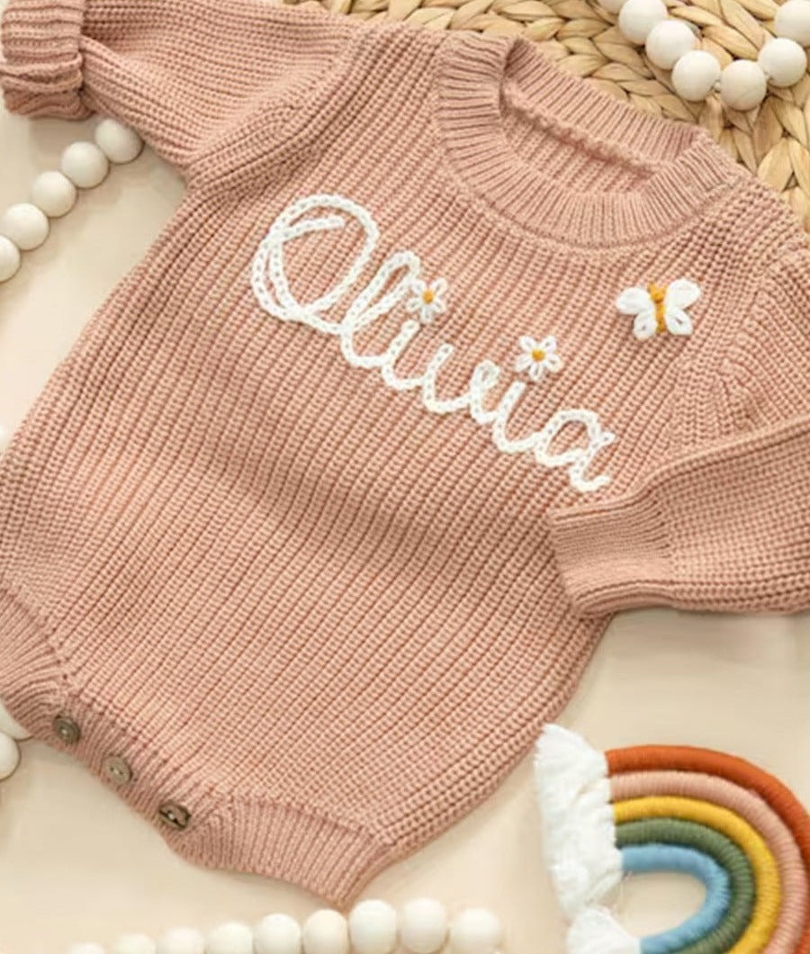 Pink knit baby romper embroidered with the name Olivia, a small flower and a butterfly