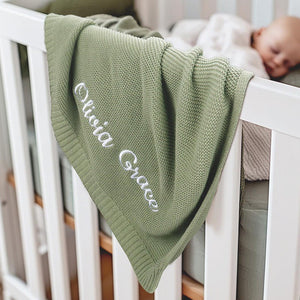 Personalized knit baby blanket draped over a crib