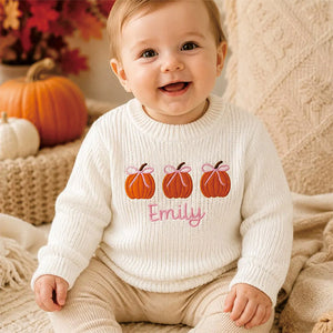 Baby in a white knit sweater embroidered with pumpkins and the name Emily