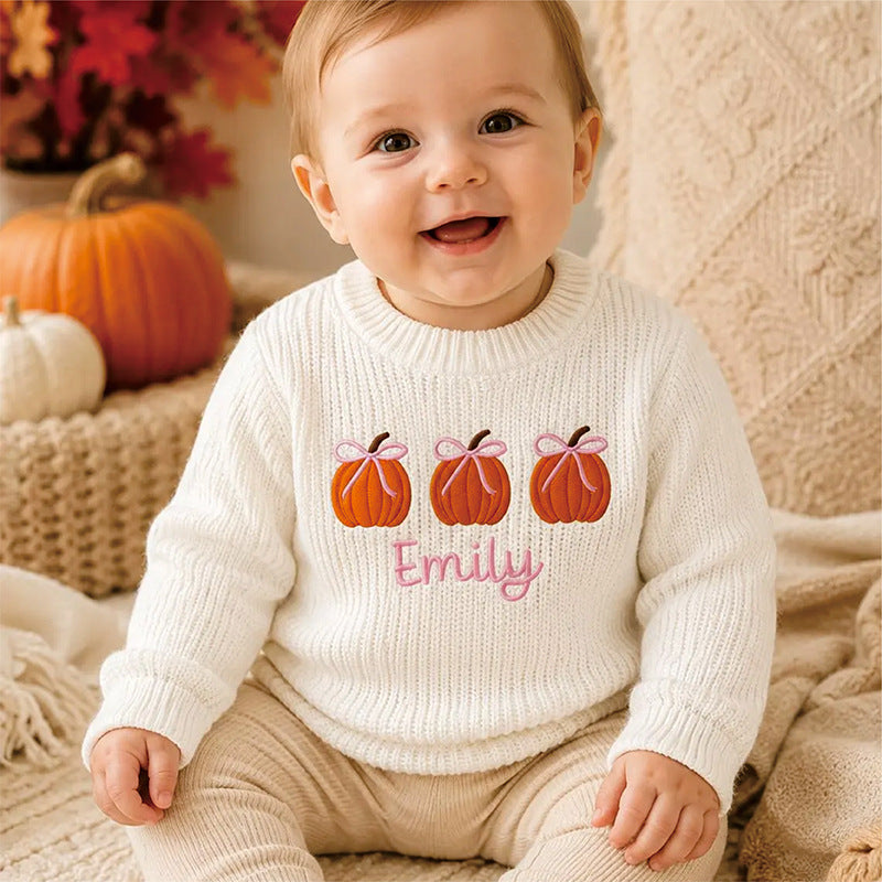 Baby in a white knit sweater embroidered with pumpkins and the name Emily