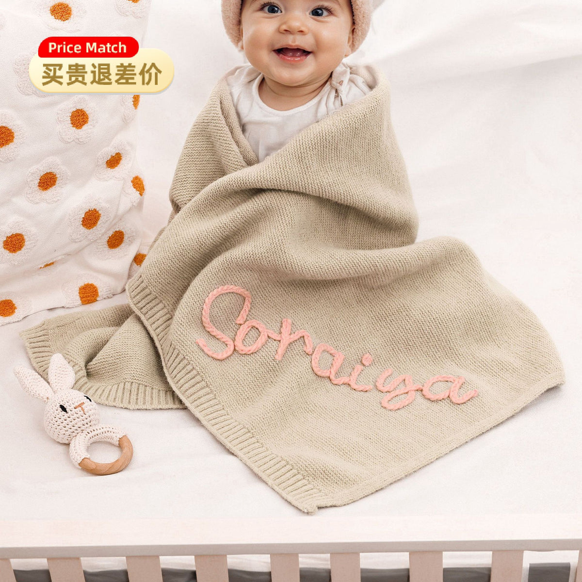 Smiling baby under a beige knit blanket embroidered with Soraiya
