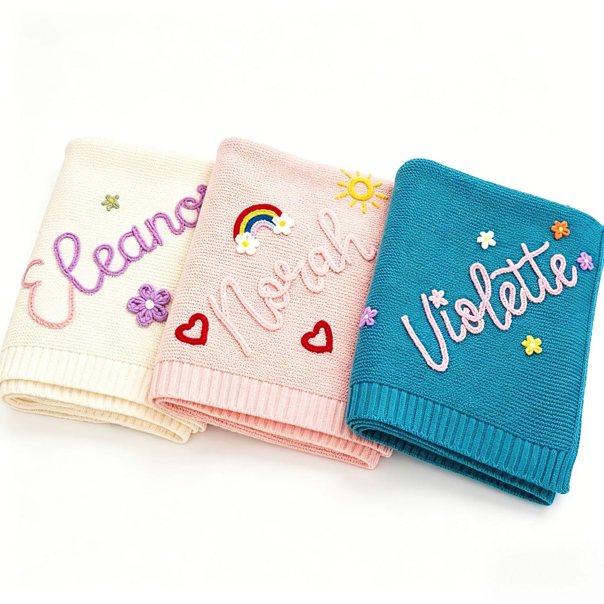 Three knit baby blankets embroidered with Eleanor, Norah and Violette with flowers and a rainbow