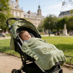 Baby in a stroller under a sage ruffle blanket embroidered with Rori