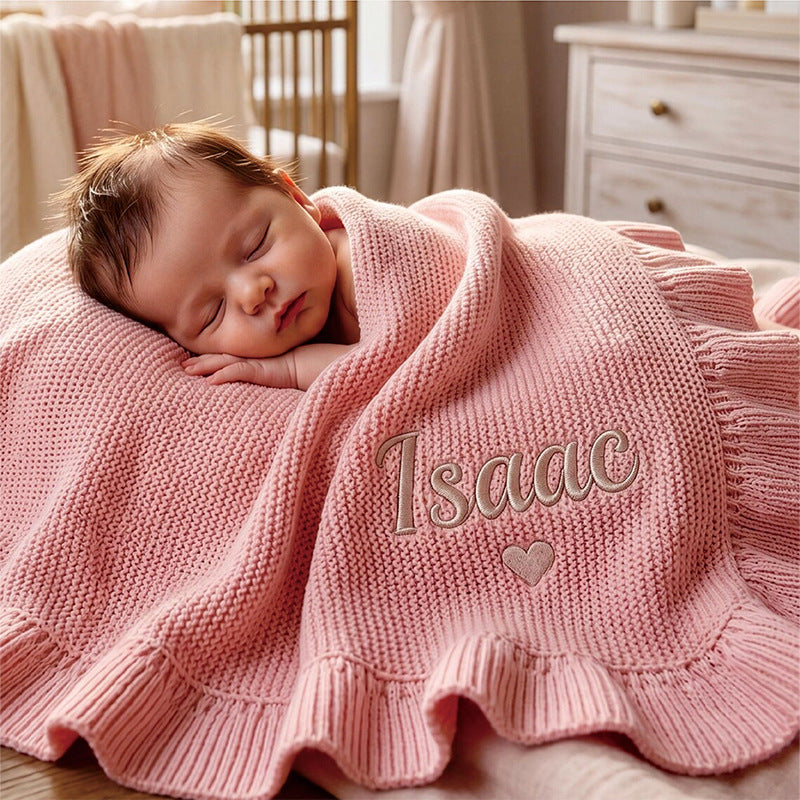 Sleeping baby under a pink ruffle blanket embroidered with Isaac