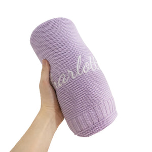 Lavender knit baby blanket rolled up with an embroidered name
