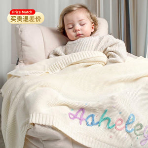 Toddler asleep under a cream knit blanket embroidered with Ashley in rainbow yarn