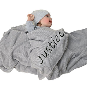 Baby under a gray knit blanket embroidered with Justice