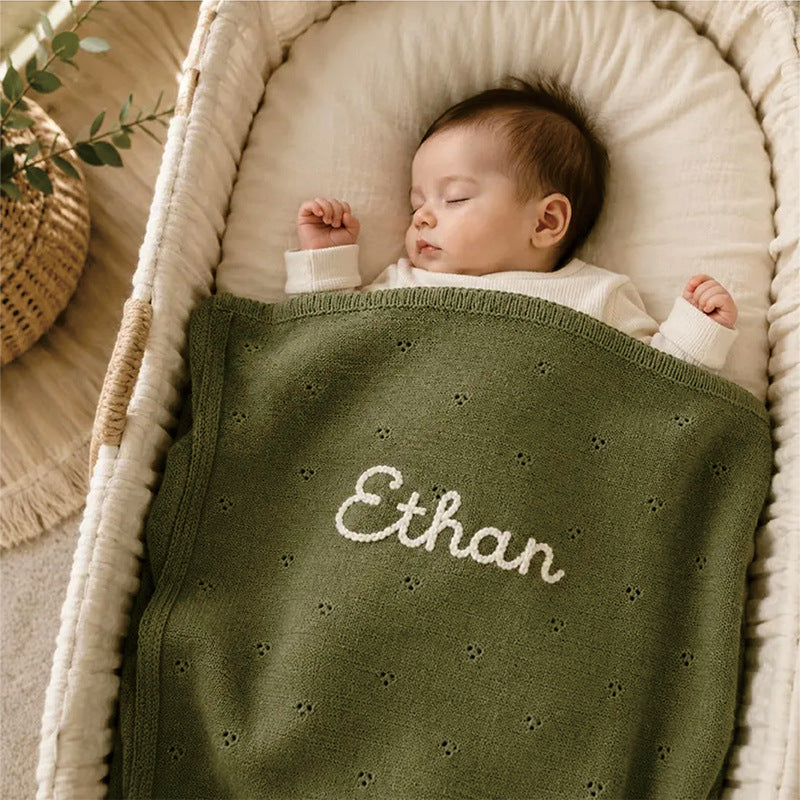 Newborn in a bassinet under a green pointelle blanket embroidered with Ethan