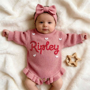 Baby in a rose pink ruffle knit romper embroidered with the name Ripley