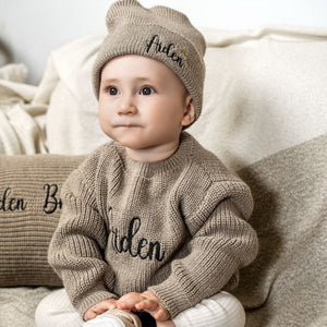 Baby wearing a chunky knit sweater with an embroidered name