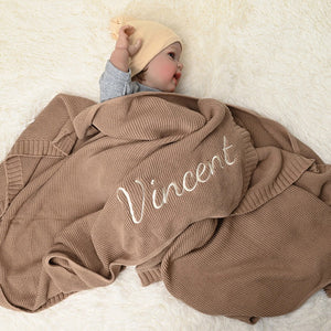 Baby under a tan knit blanket embroidered with Vincent