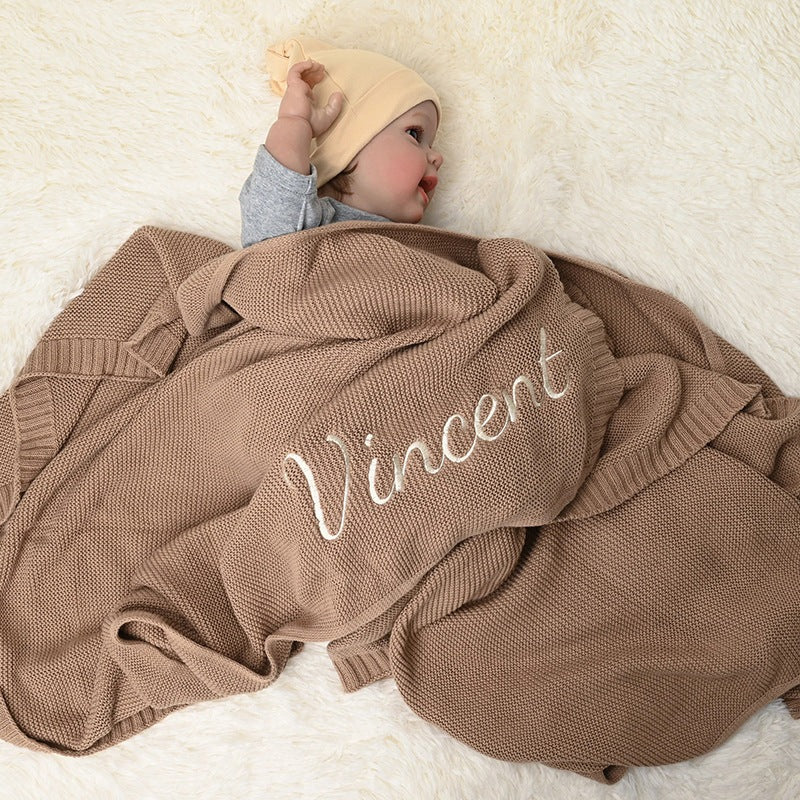 Baby under a tan knit blanket embroidered with Vincent