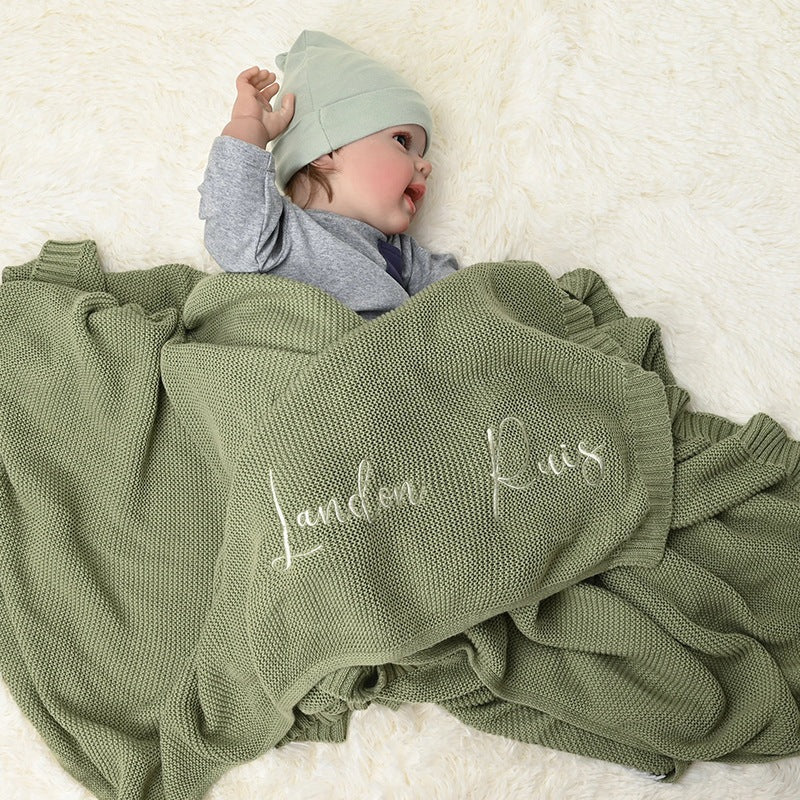 Baby under a sage knit blanket embroidered with Landon Ruis