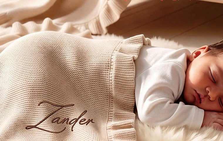 Baby under a cream ruffle blanket embroidered with Zander