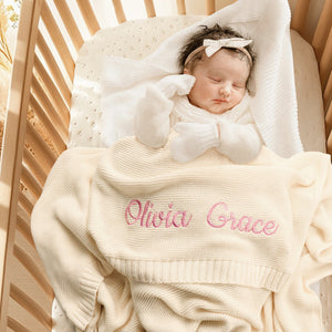 Newborn under a cream knit blanket embroidered with Olivia Grace