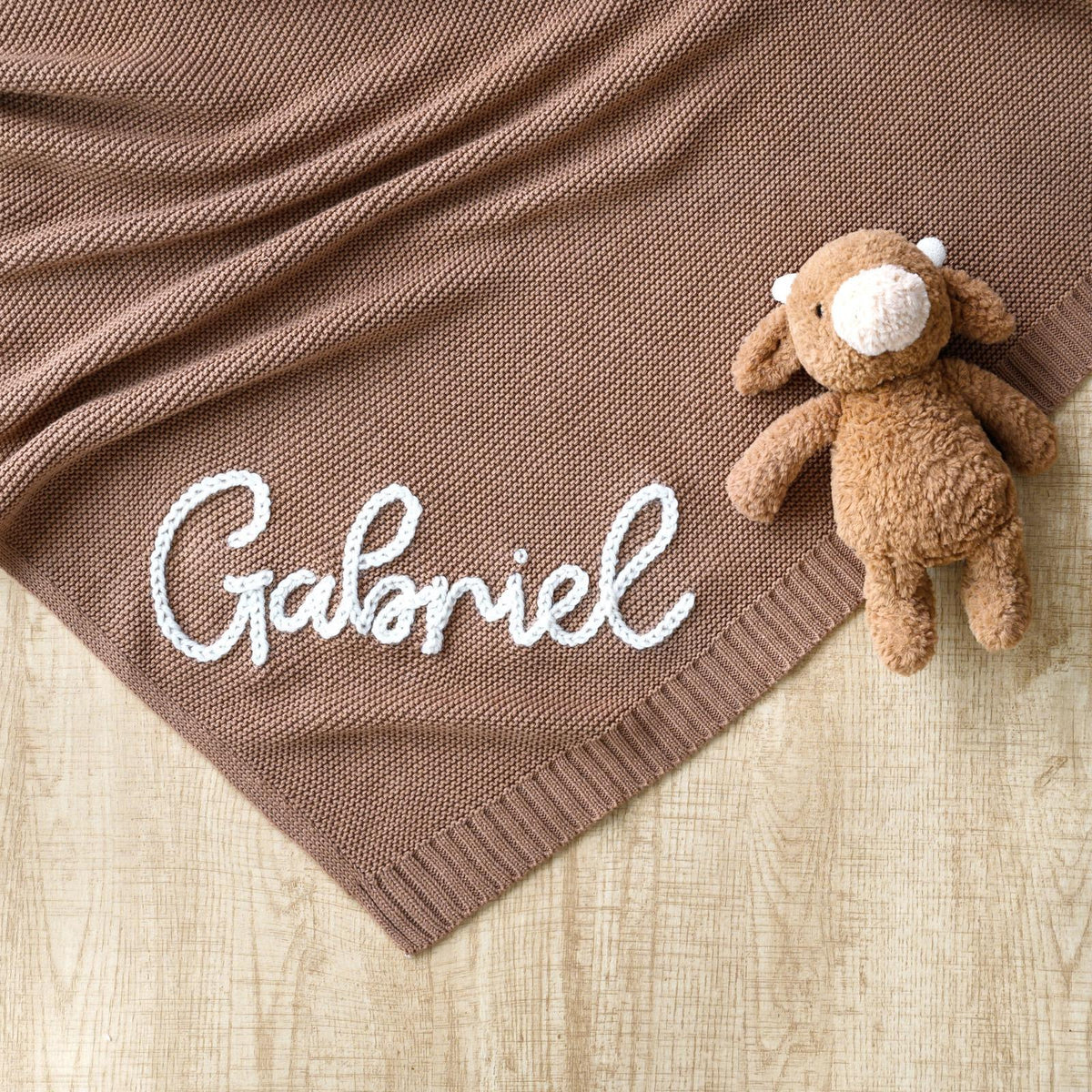 Brown knit blanket embroidered with Gabriel next to a teddy bear