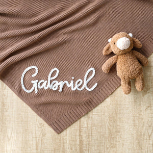 Brown knit blanket embroidered with Gabriel next to a teddy bear