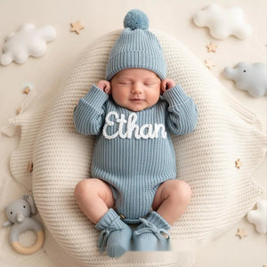 Newborn in a gray blue knit romper and hat embroidered with the name Ethan