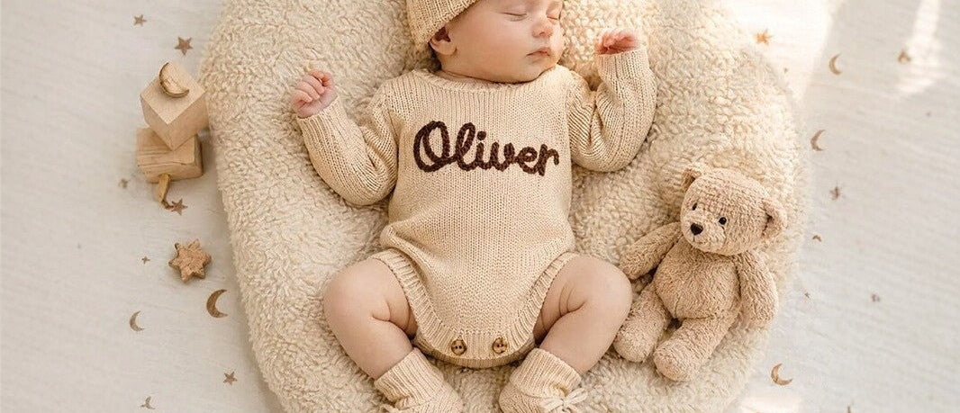 Newborn in an oatmeal knit romper embroidered with the name Oliver