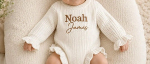 Baby wearing a cream ruffle knit romper embroidered with Noah James