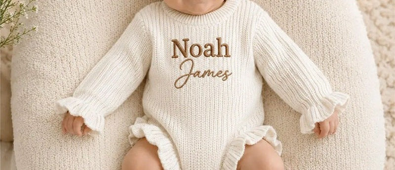 Baby wearing a cream ruffle knit romper embroidered with Noah James