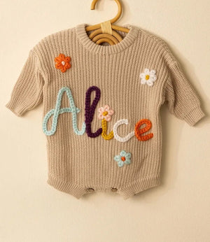Beige knit baby romper embroidered with the name Alice in colorful yarn with small flowers