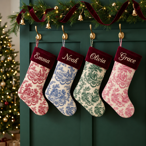 Personalized toile Christmas stockings with burgundy velvet cuff hanging by the fireplace